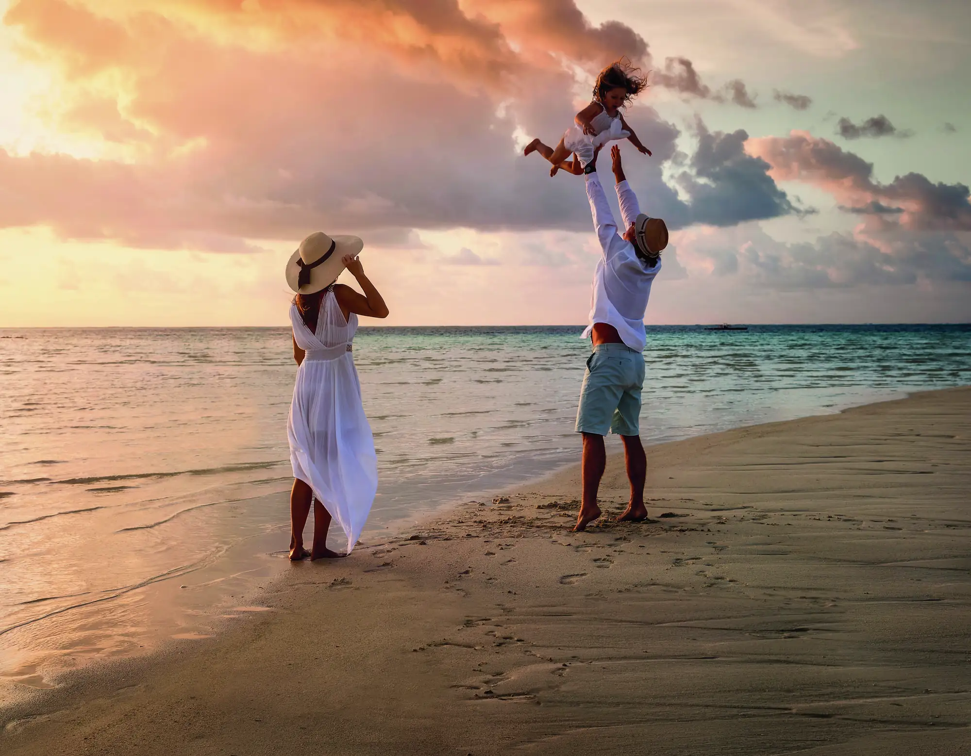 Parents playing with their young child on a beach at sunset